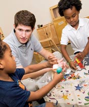 Erikson alumnus working with two children playing at a sandbox