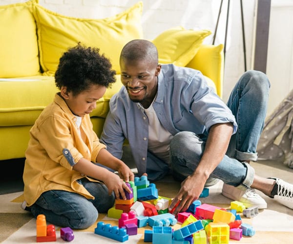 smiling african american father and little son playing with colorful blocks together at home