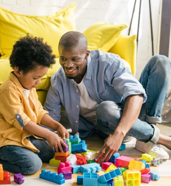 smiling african american father and little son playing with colorful blocks together at home