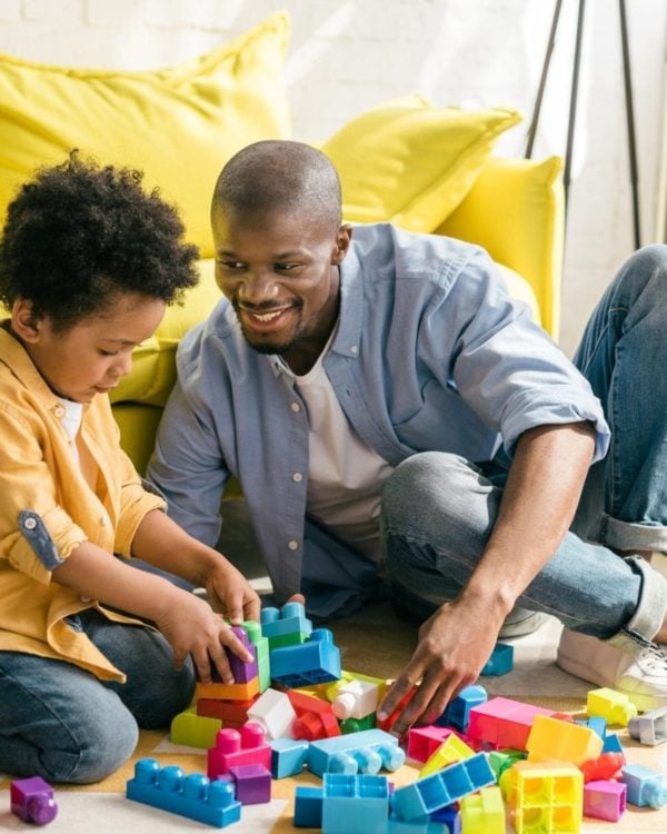 smiling african american father and little son playing with colorful blocks together at home