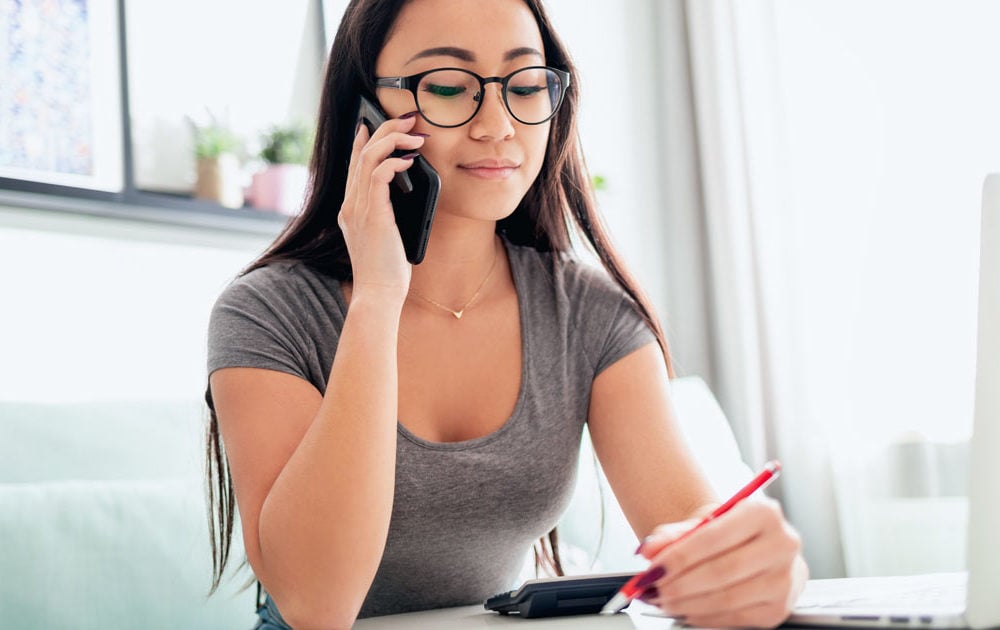 Woman seated at a desk talking on a smartphone.