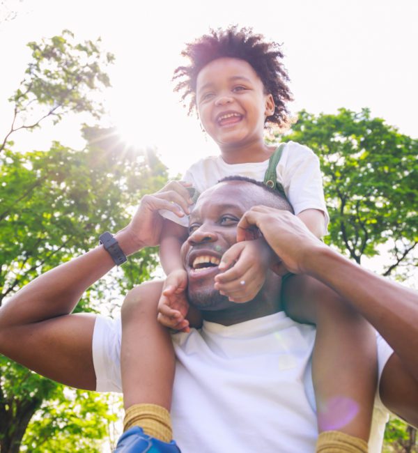 African American father giving son ride on back at park. family playing togetherness and relaxes. Family weekend. Cute African American boy with dad playing outdoor.