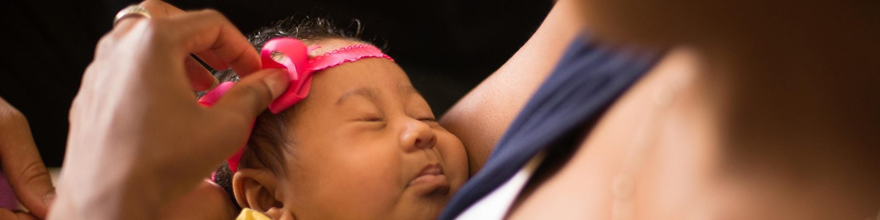 Mother holding a sleeping infant while placing a bow on her baby’s head.