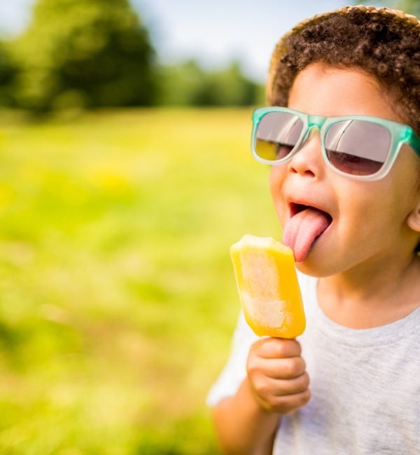 Boy in sunglasses and hat eating popsicle outdoors