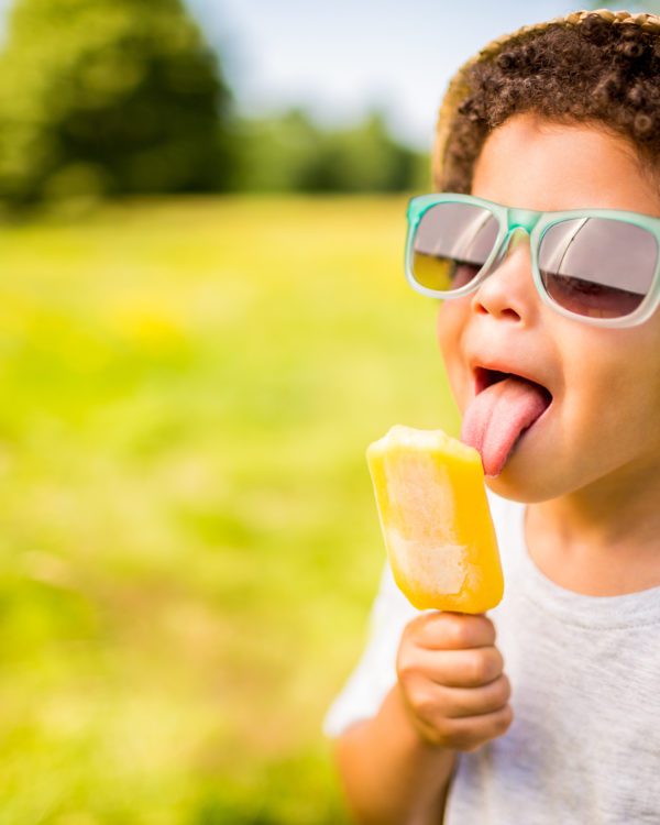 Boy in sunglasses and hat eating popsicle outdoors