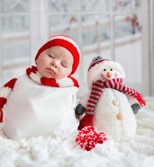 Christmas portrait of cute little newborn baby boy, wearing santa hat and little cute snowman toy, studio shot, winter time