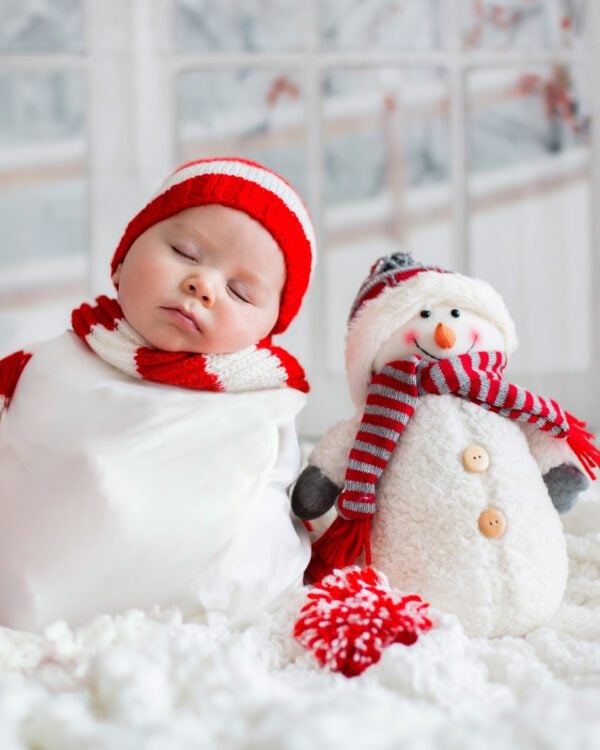 Christmas portrait of cute little newborn baby boy, wearing santa hat and little cute snowman toy, studio shot, winter time