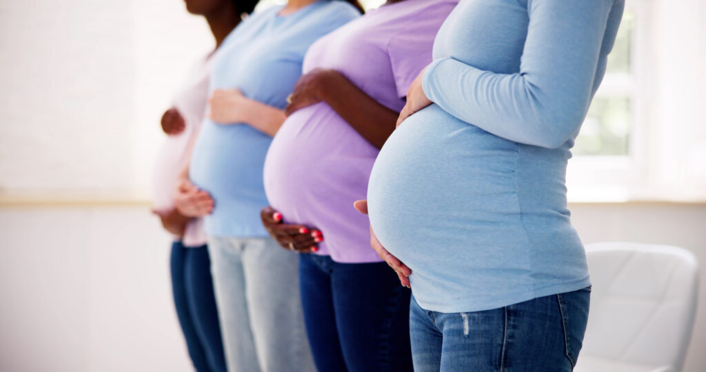 four pregnant women standing in a row with their hands supporting their stomachs