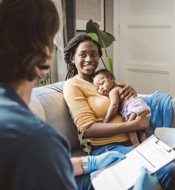 A woman holding a baby talking to a professional