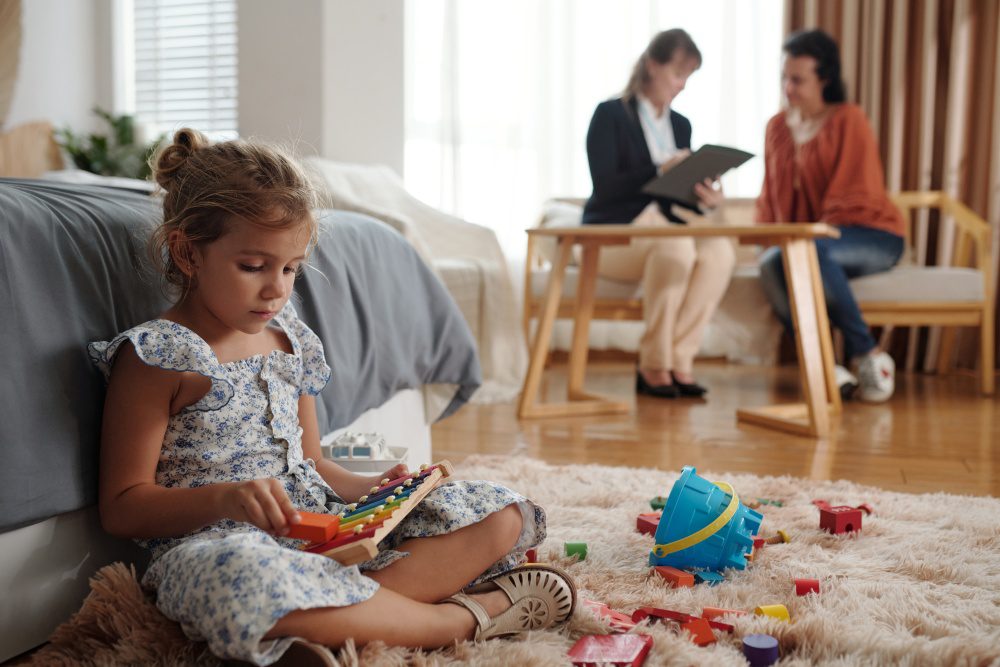 female home visitor or early interventionist sitting with a young child and parent in a home setting